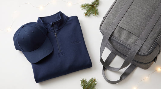 Flat lay of branded corporate holiday gifts including an embroidered quarter-zip pullover, a cap, and a cooler bag