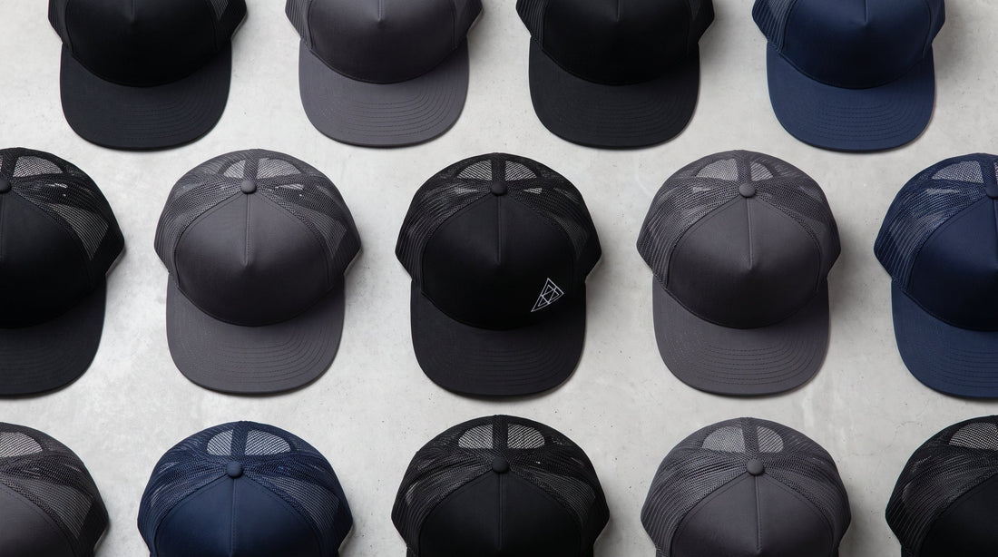Custom flat bill hats in black, charcoal, and navy with embroidered logo, arranged flat lay style