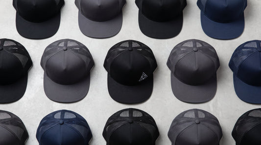 Custom flat bill hats in black, charcoal, and navy with embroidered logo, arranged flat lay style