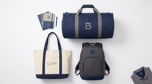 Custom embroidered bags for business — tote bag, backpack, and duffel bag flat lay in navy and grey