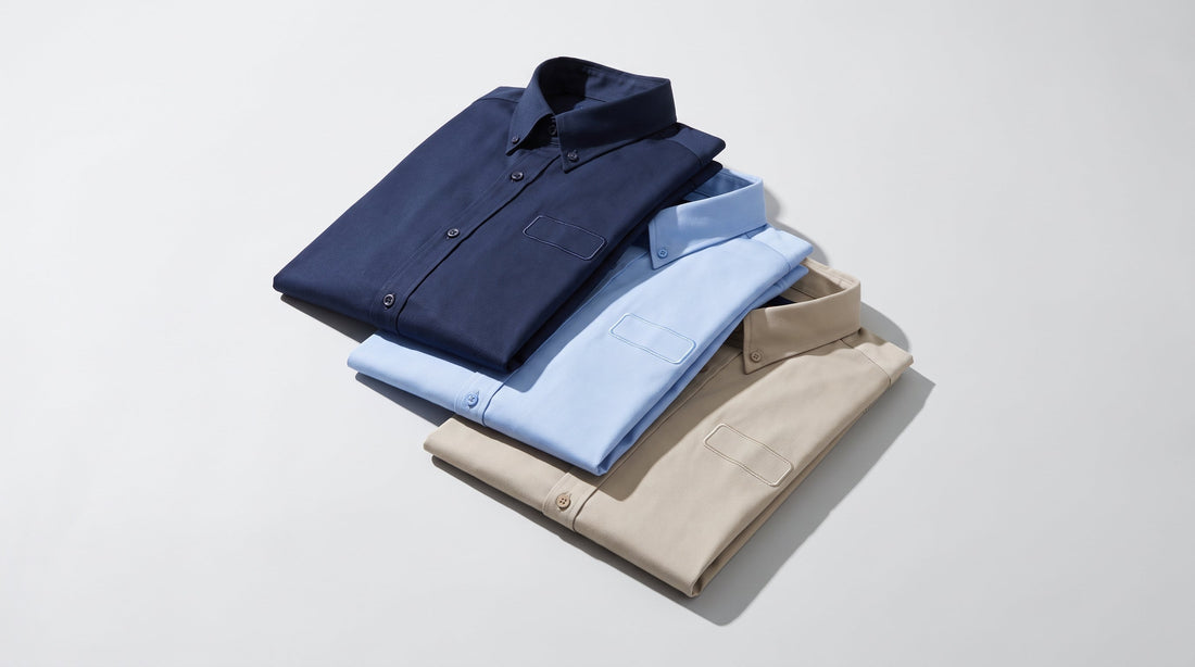 Folded navy, light blue, and stone corporate button-down work shirts stacked for custom logo embroidery
